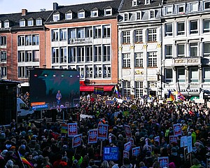 Große Menschenmasse steht mit Demoschildern auf dem Aachener Markt. Auf einem großen Bildschirm ist die Oberbürgermeisterin Sybille Keupen zu sehen.